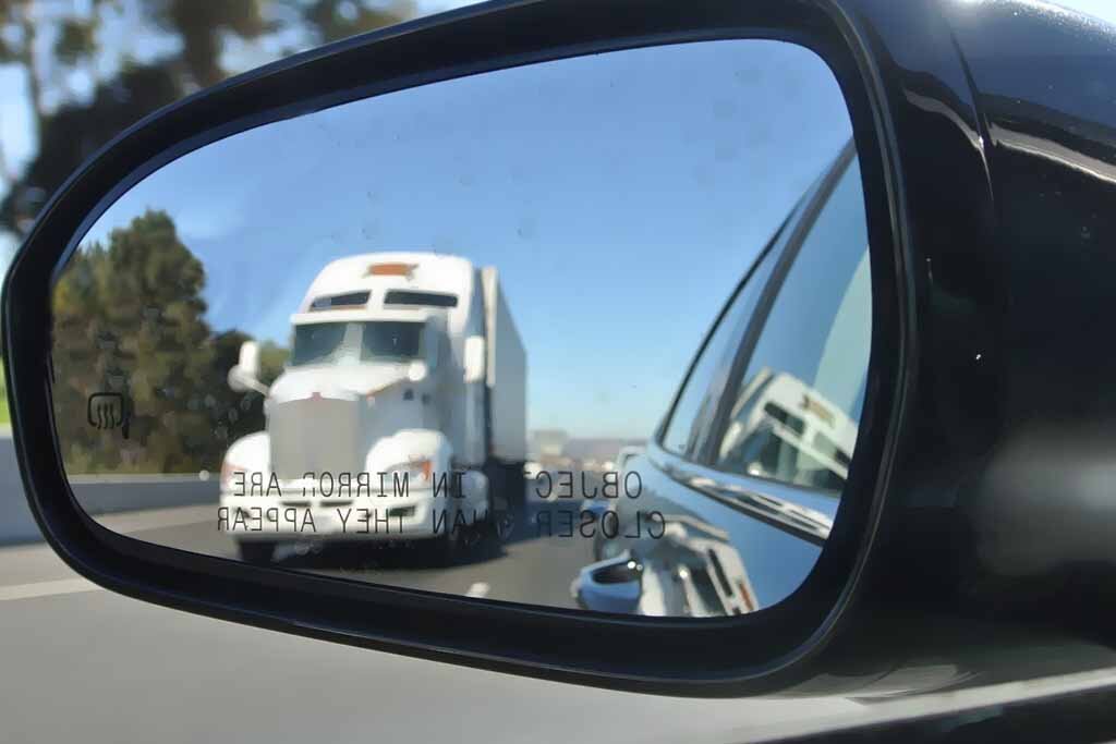 auto transport truck in side mirror driving on the interstate
